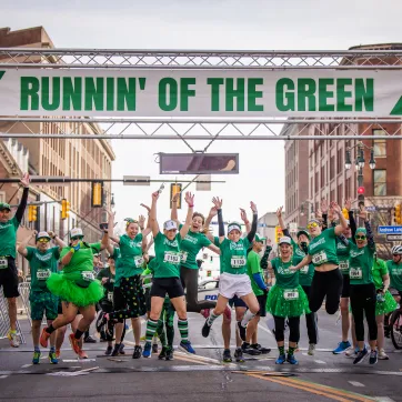 People jumping and celebrating a the finish line at Runnin' of the Green race.