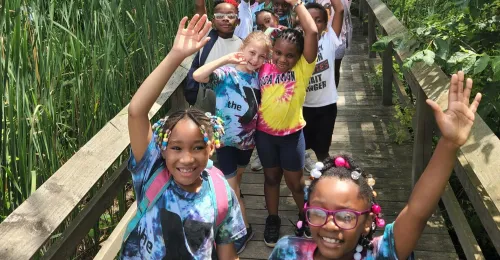 A group of kids from power scholars walking on a wooden walking bridge outside