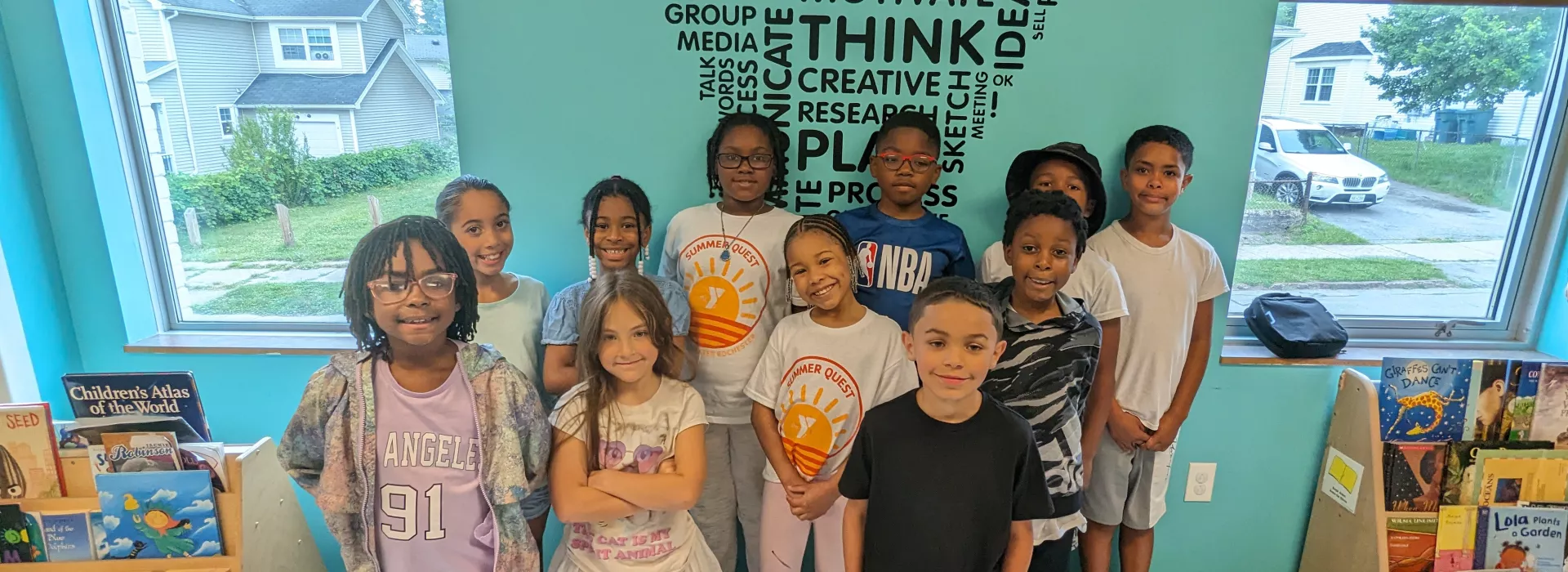 a group of 11 kids standing in front of a wall with a word cloud that has words like: create, strategy, innovate, think, motivate, positive, goal, power, etc