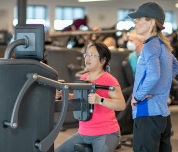 ymca member works out on egym equipment while staff helps give tips