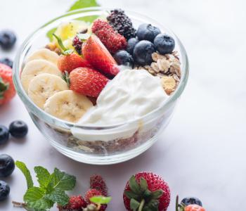 a smoothie bowl with bananas, strawberries, blueberries and granola in a glass bowl on a marble table