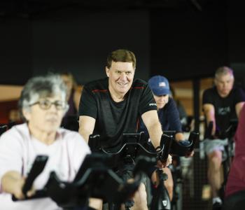 Man smiles while cycling in a YMCA group exercise class