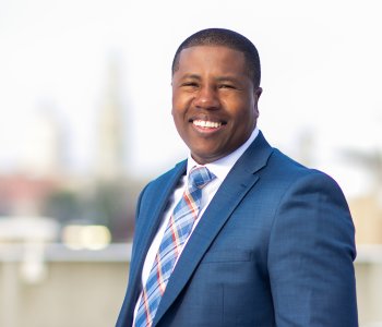 Ernie Lamour, President & CEO, YMCA of Greater Rochester, smiles with the skyline of City of Rochester behind him