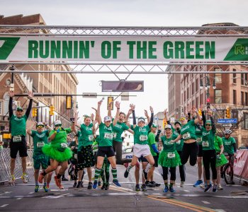 People jumping and celebrating a the finish line at Runnin' of the Green race.