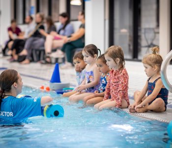 a swim instructor is in the pool speaking with a group of five young swimmers during a swim lesson